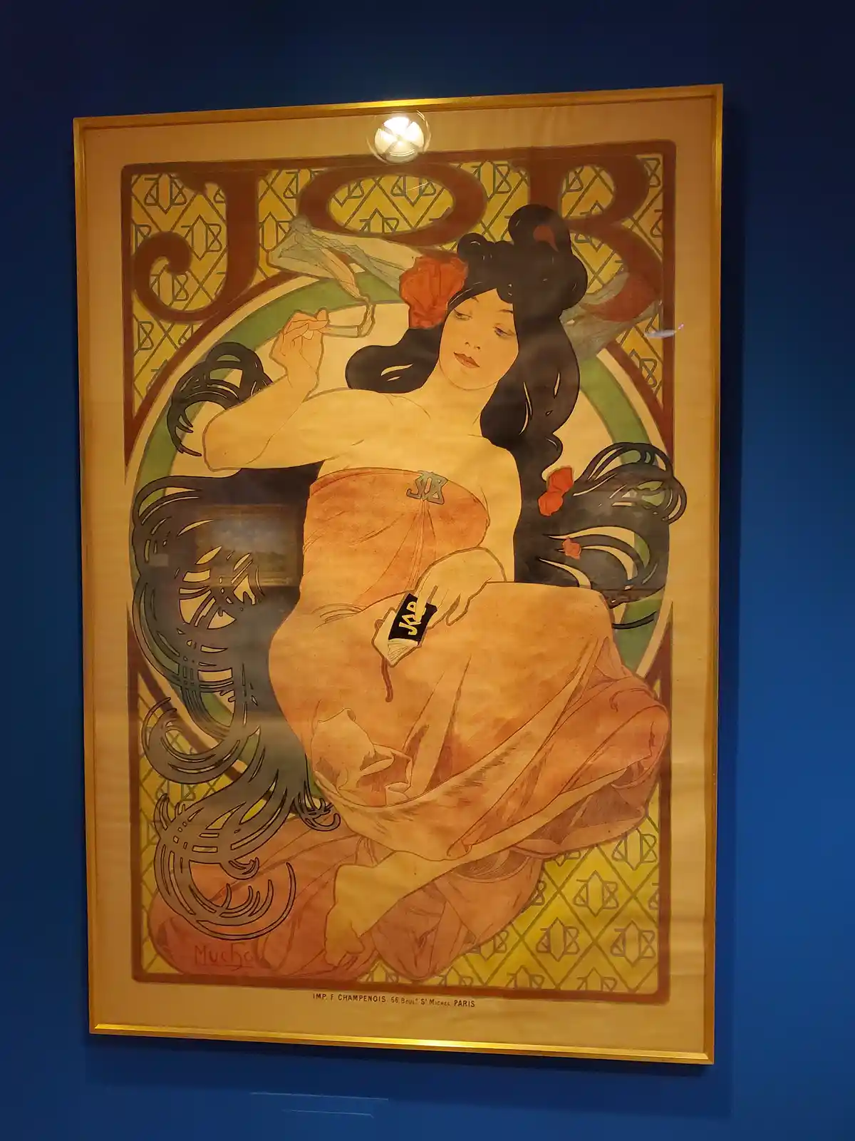 A framed Art Nouveau poster by Mucha depicting a reclining woman with long black hair adorned with red flowers, holding a…