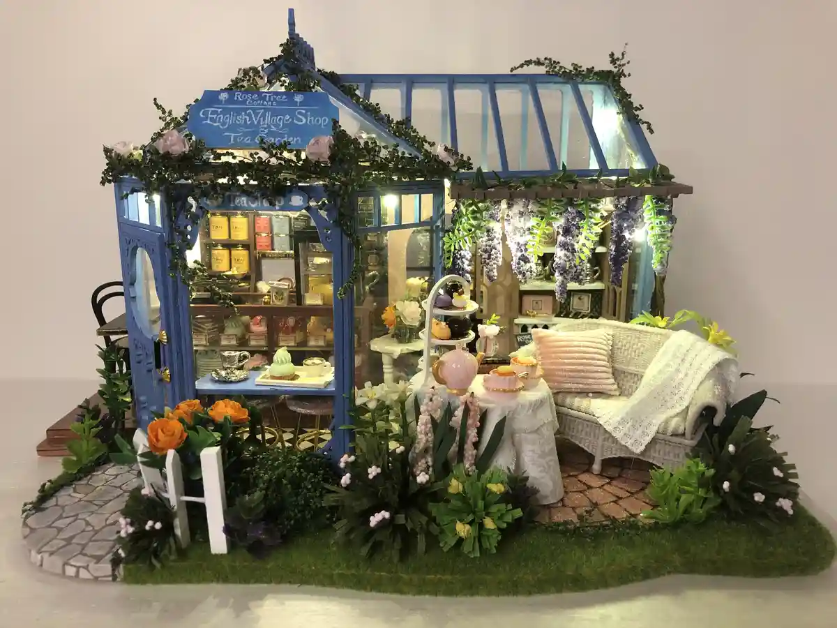A miniature, intricately detailed dollhouse-style tea shop with blue framing, glass panels, and a sign reading 'Rose Tree…