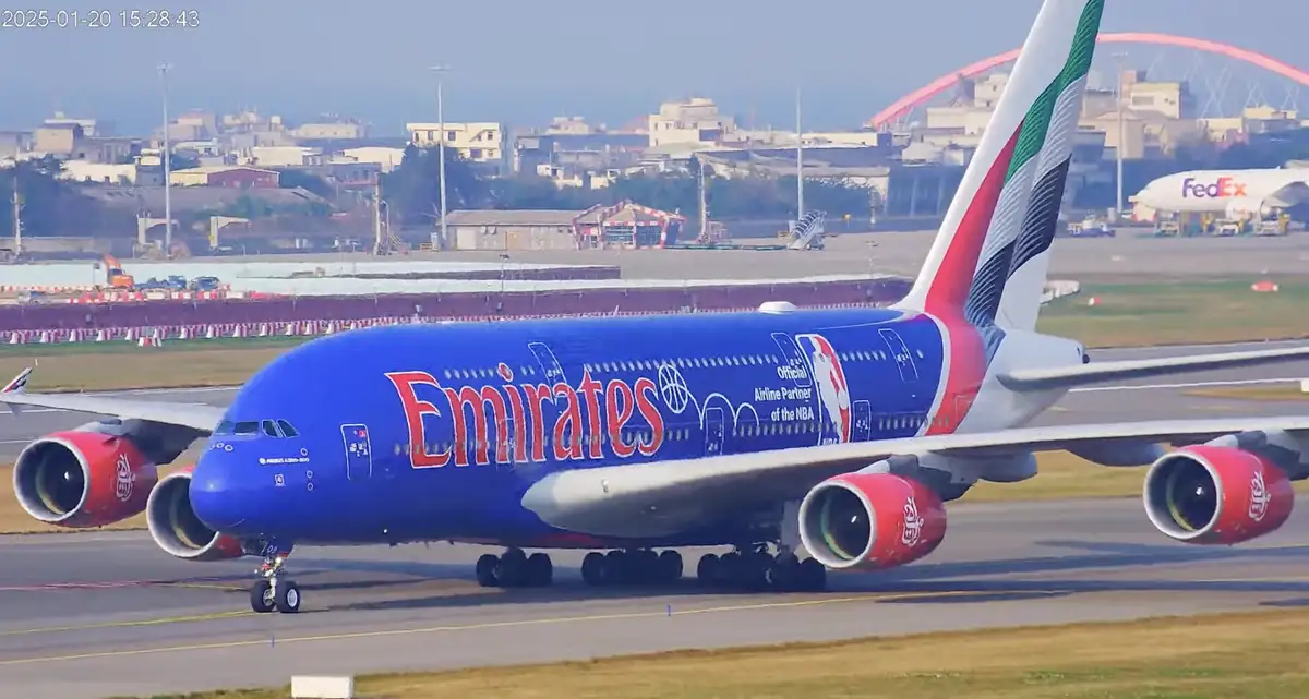 A large blue Emirates Airbus A380 airplane with red engines and 'Official Airline Partner of the NBA' livery is taxiing on…