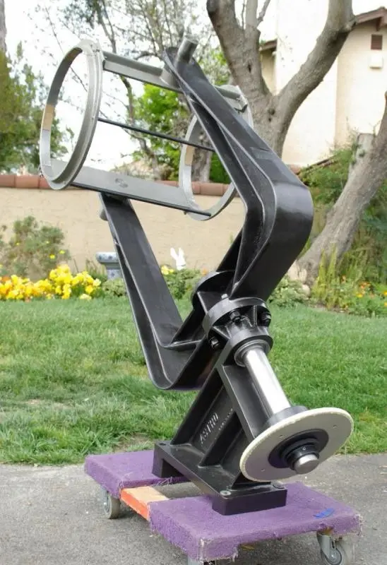 A large, black, industrial-looking steering wheel assembly sits on a purple dolly in a grassy yard. The overlaid text reads…