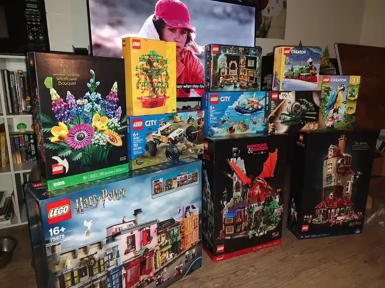 A collection of large LEGO set boxes, including Harry Potter, Dungeons & Dragons, and City themes, are stacked on a wooden…