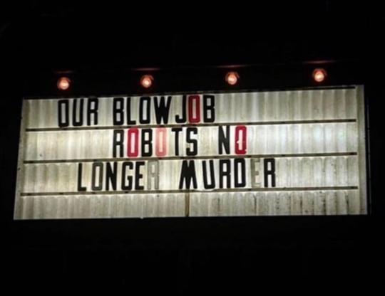 A weathered, illuminated theater marquee displays the text 'OUR BLOWJOB ROBOTS NO LONGER MURDER' in black and red letters…