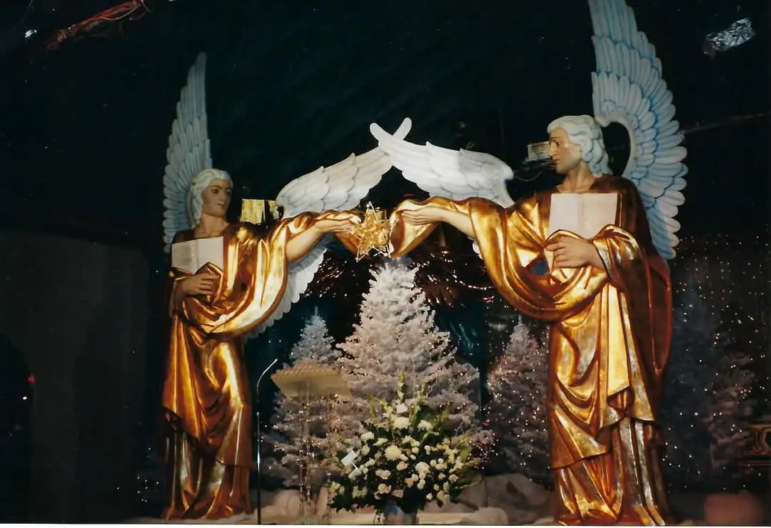 Two golden angel statues with large white wings stand facing each other, each holding one side of a glowing star-shaped…