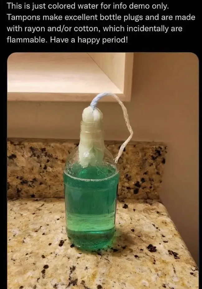 A clear glass bottle filled with green liquid sits on a speckled countertop, plugged at the neck with a white tampon. The…