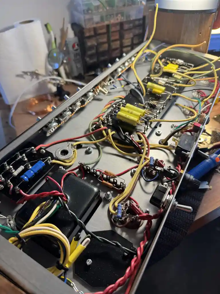 A close-up photo of a cluttered electronics workbench showing a partially assembled circuit board with numerous colorful…