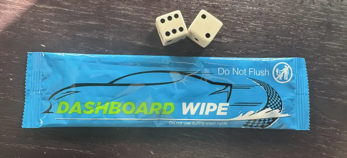 A blue packaged dashboard wipe with a car silhouette and racing checkered flag design lies on a dark wooden surface, with…