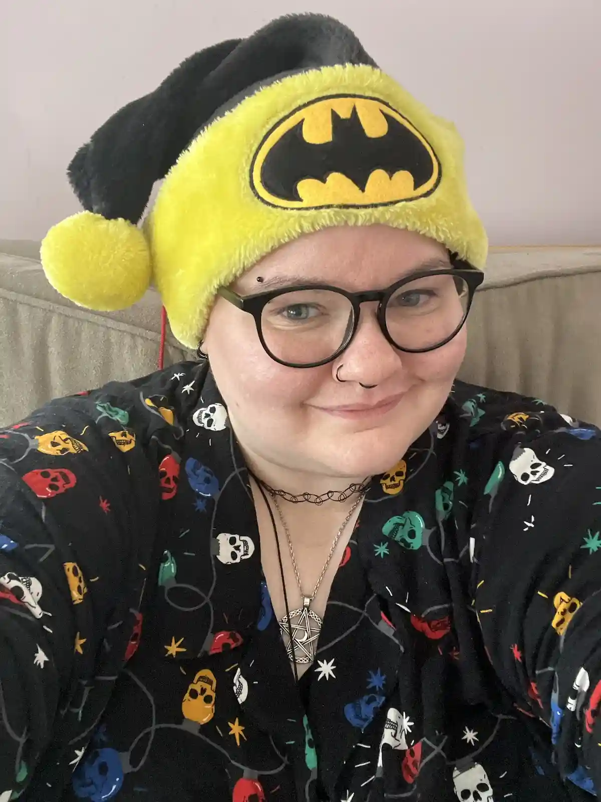 A person wearing a yellow and black Batman-themed jester hat with a pom-pom, black-rimmed glasses, and a black shirt covered…