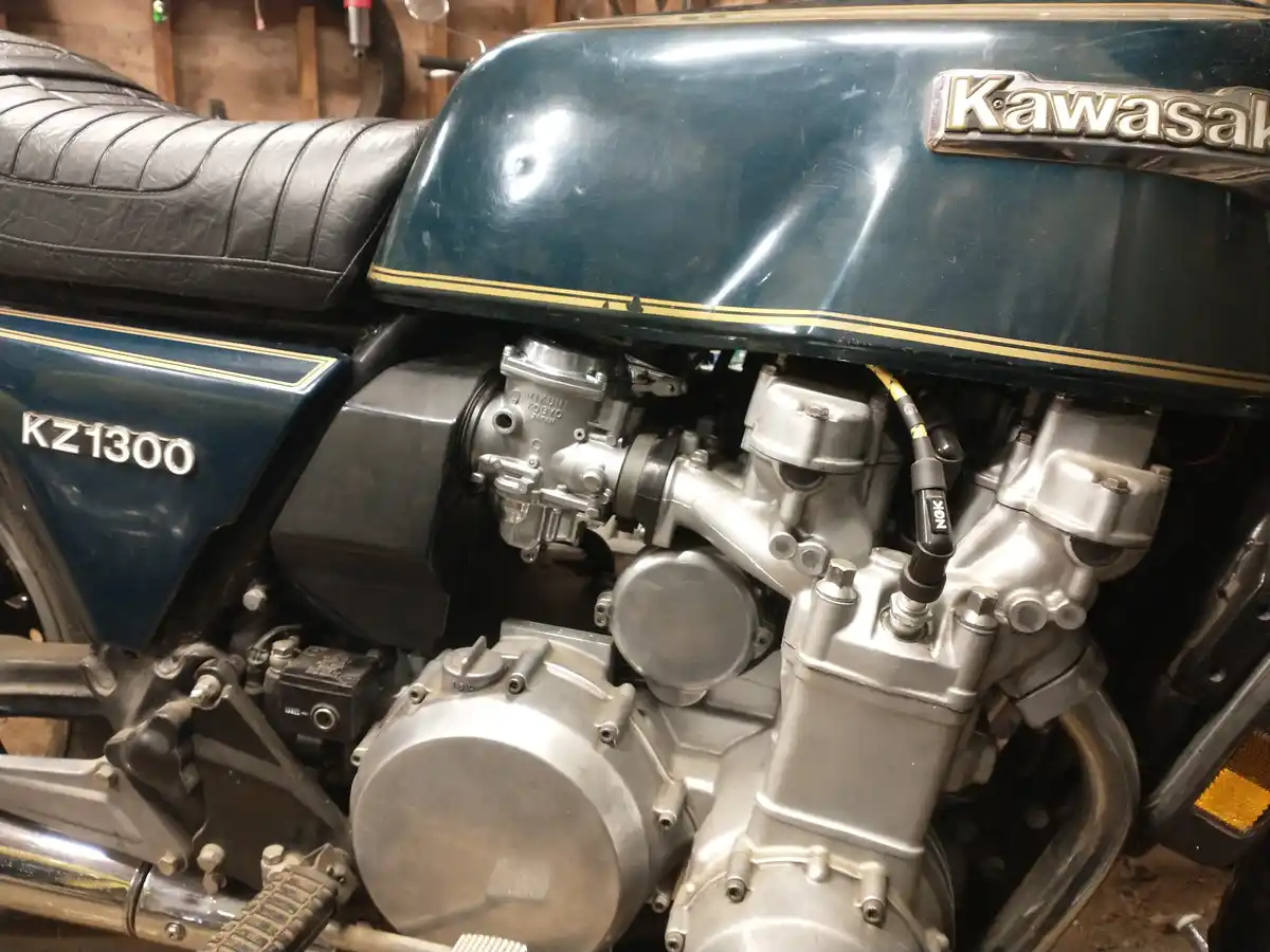 A close-up photo of a vintage Kawasaki KZ1300 motorcycle engine, showing its chrome components, black leather seat, and…