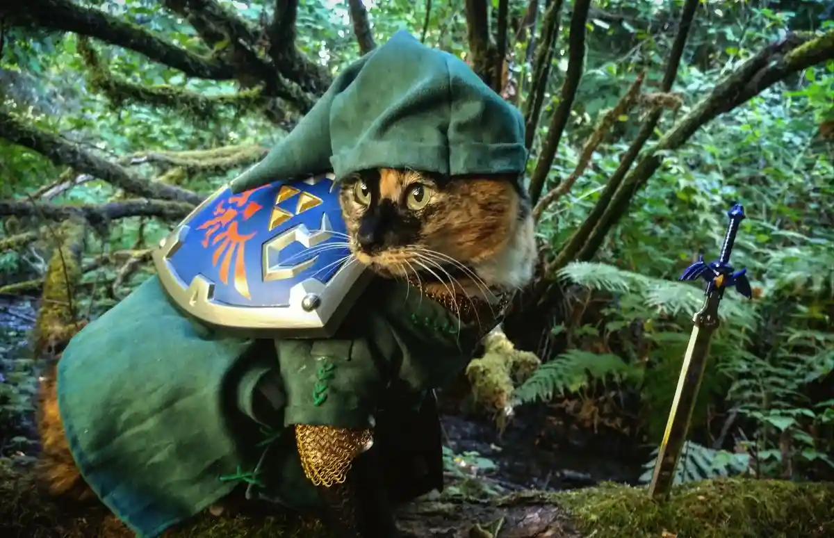 A calico cat dressed in a green Link costume from The Legend of Zelda, holding a Hylian Shield and standing beside a Master…
