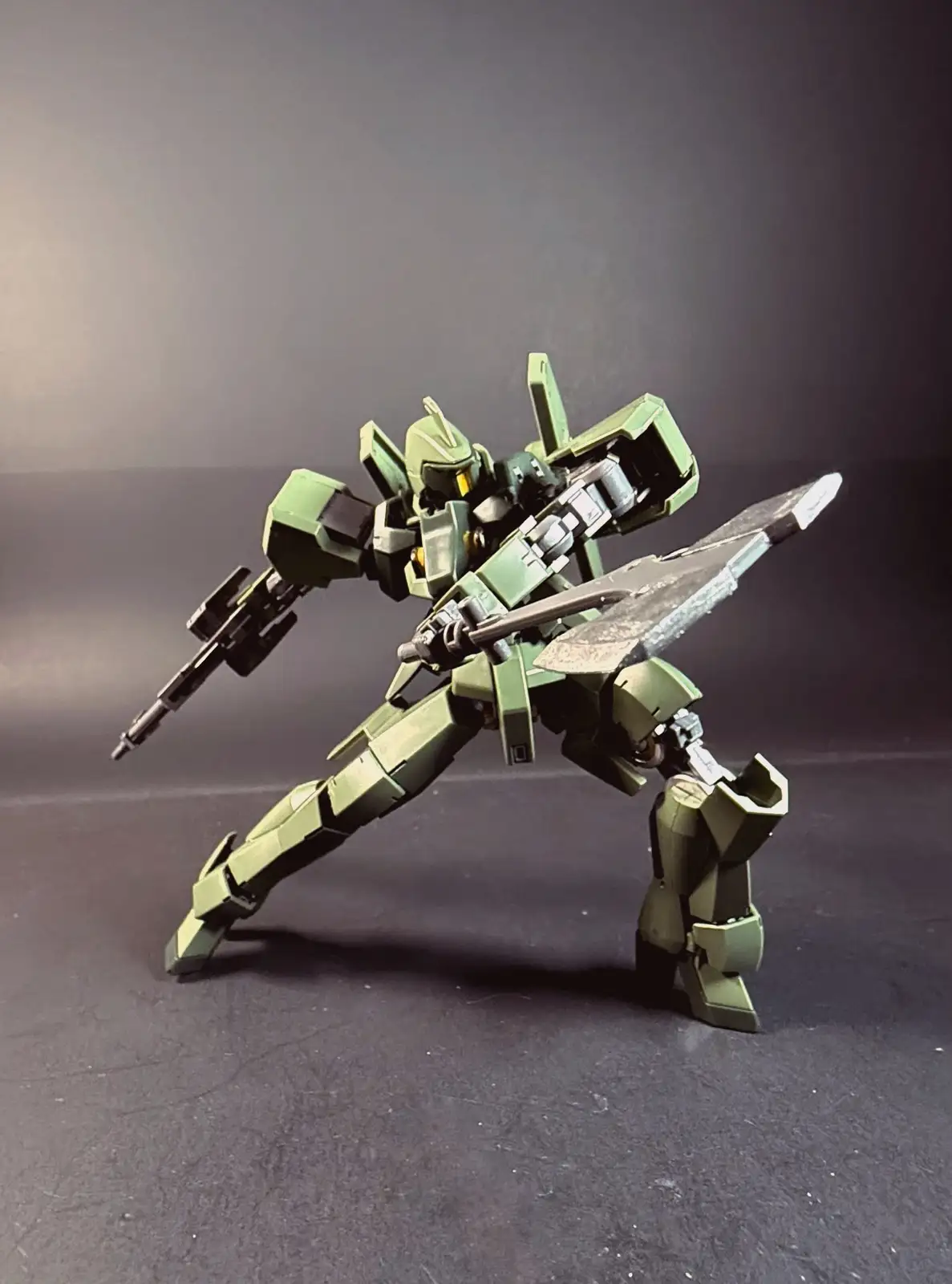 A green, angular, humanoid robot model stands in a dynamic combat pose against a dark gray background, holding a large sword…