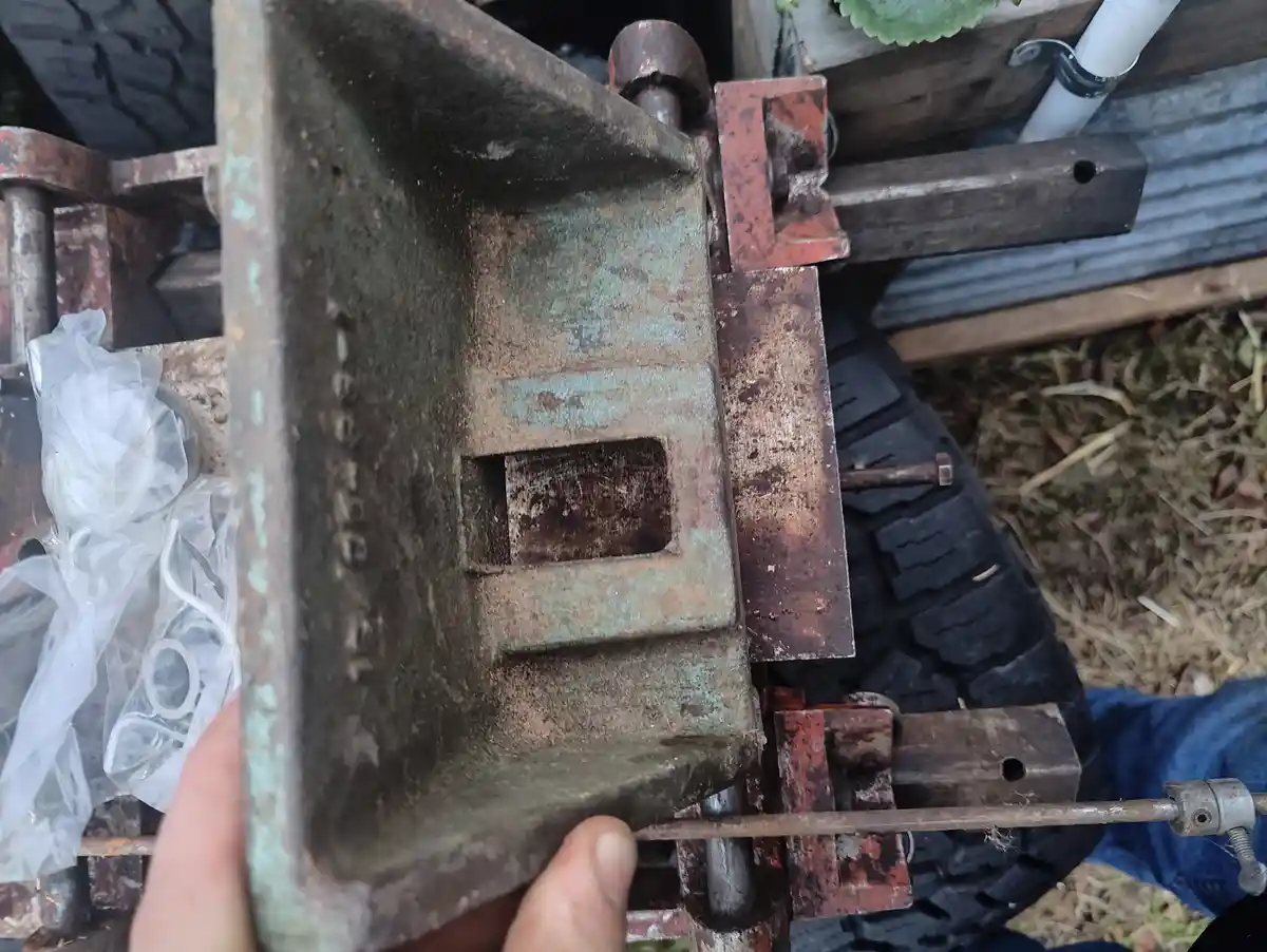 A close-up photo shows a person holding a rusty, weathered metal tractor part with visible greenish corrosion and faded…