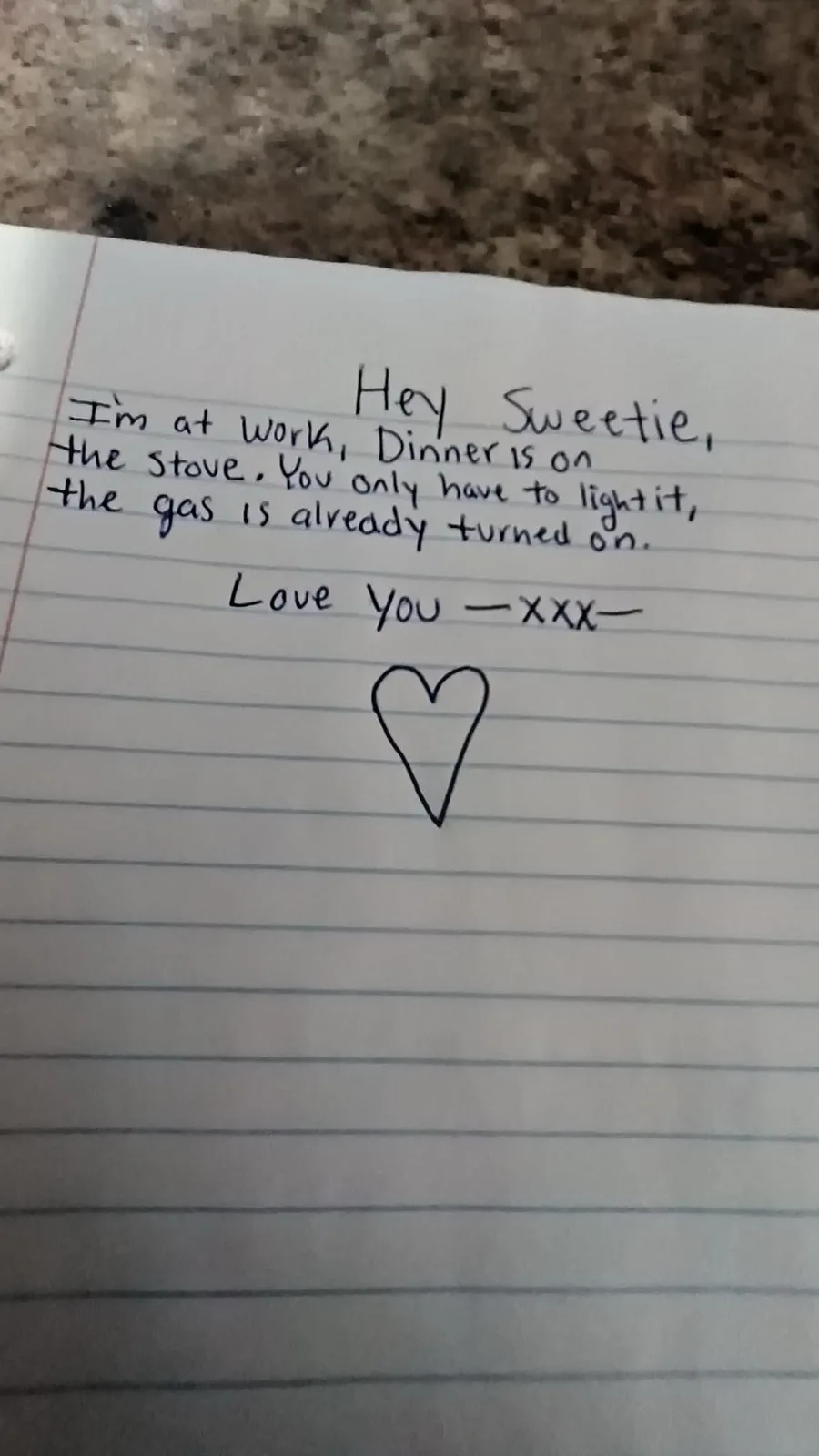 A handwritten note on lined paper reads a sweet message to a partner, saying dinner is on the stove and the gas is already…