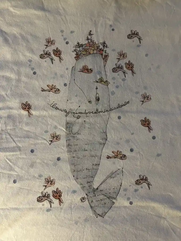 A t-shirt graphic shows a large, stylized fish with a small village of colorful houses perched on its back, surrounded by…