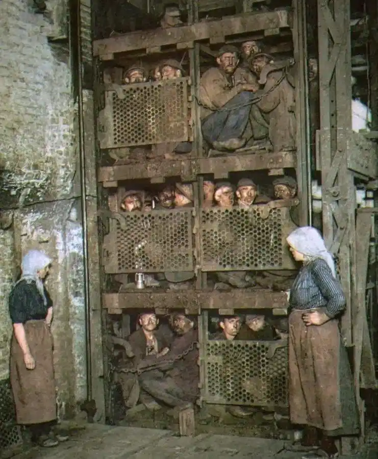 A historical photograph shows a cramped, multi-level wooden elevator shaft packed with numerous men, many looking out…