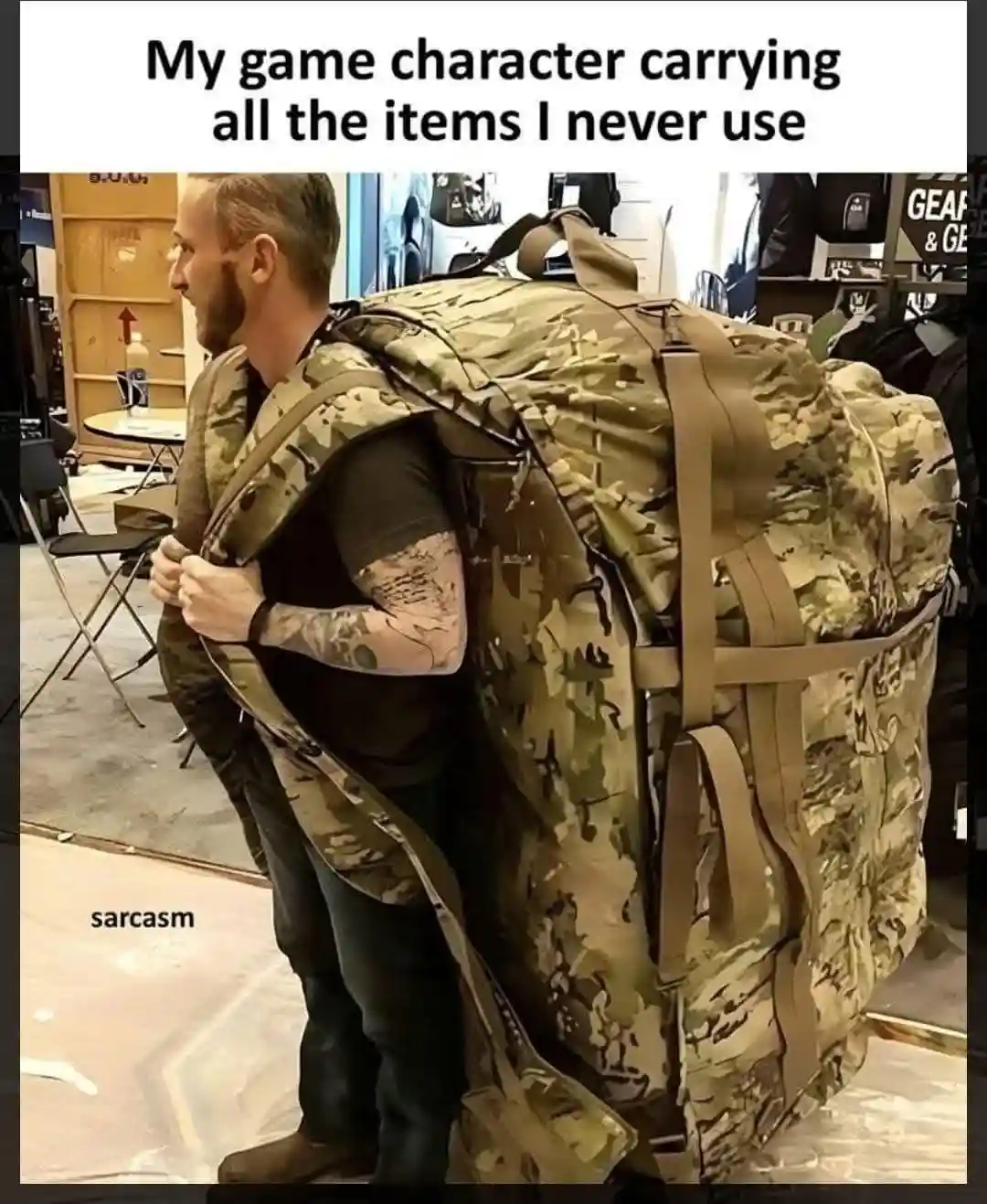 A man with a beard and tattooed arm is seen from the side, struggling under an enormous, overstuffed camouflage backpack…