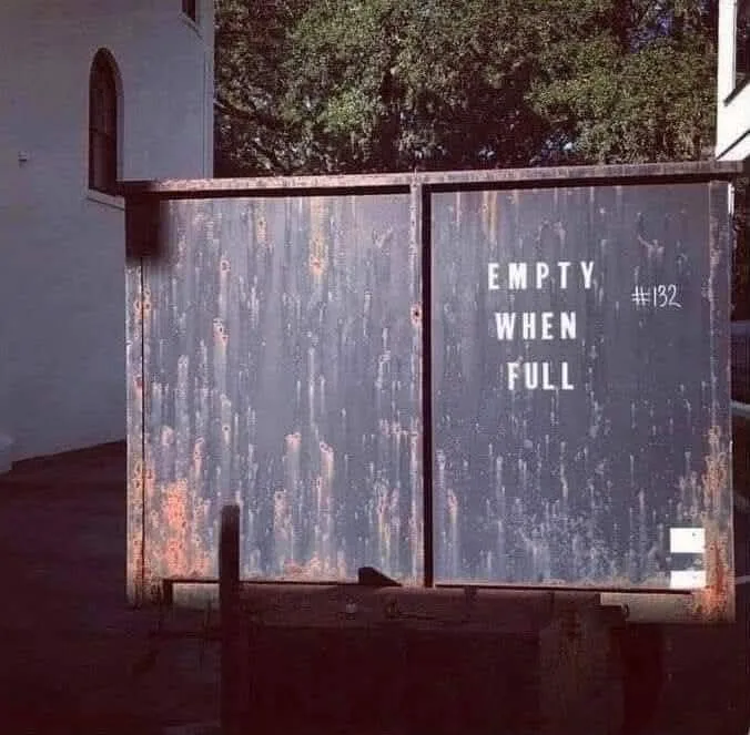 A rusty, weathered metal gate or dumpster door with peeling paint and visible rust streaks. White text is stenciled on the…