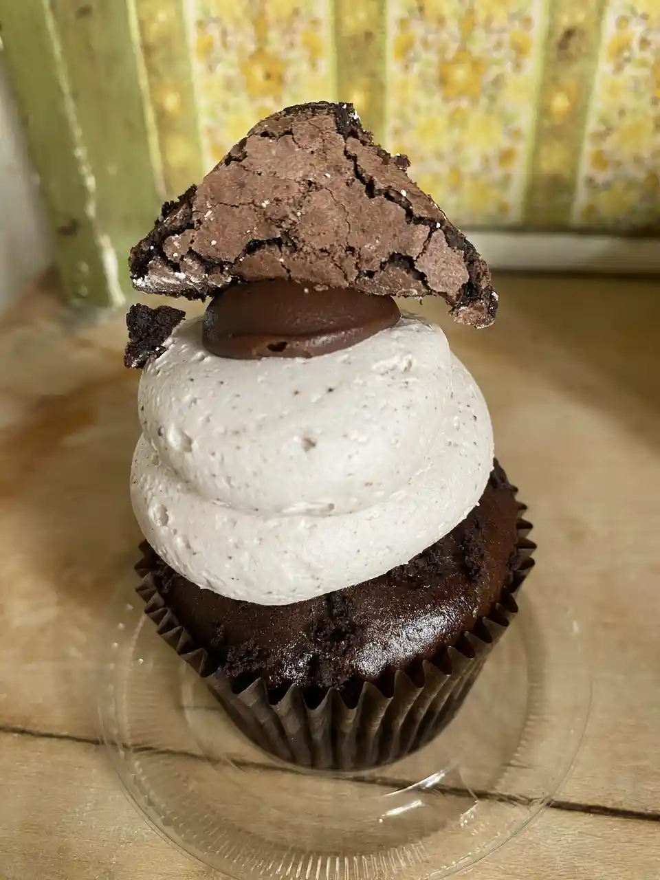 A chocolate cupcake with white frosting and a chocolate brownie piece on top, arranged to resemble a mushroom. The text…
