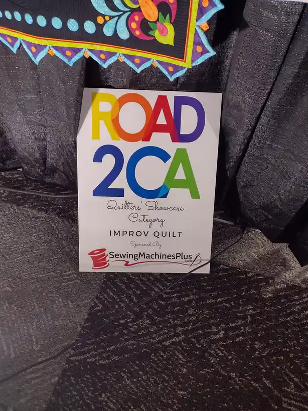 A white sign with colorful, rainbow-gradient text reading 'ROAD 2CA' sits on a dark carpeted floor, partially obscured by…