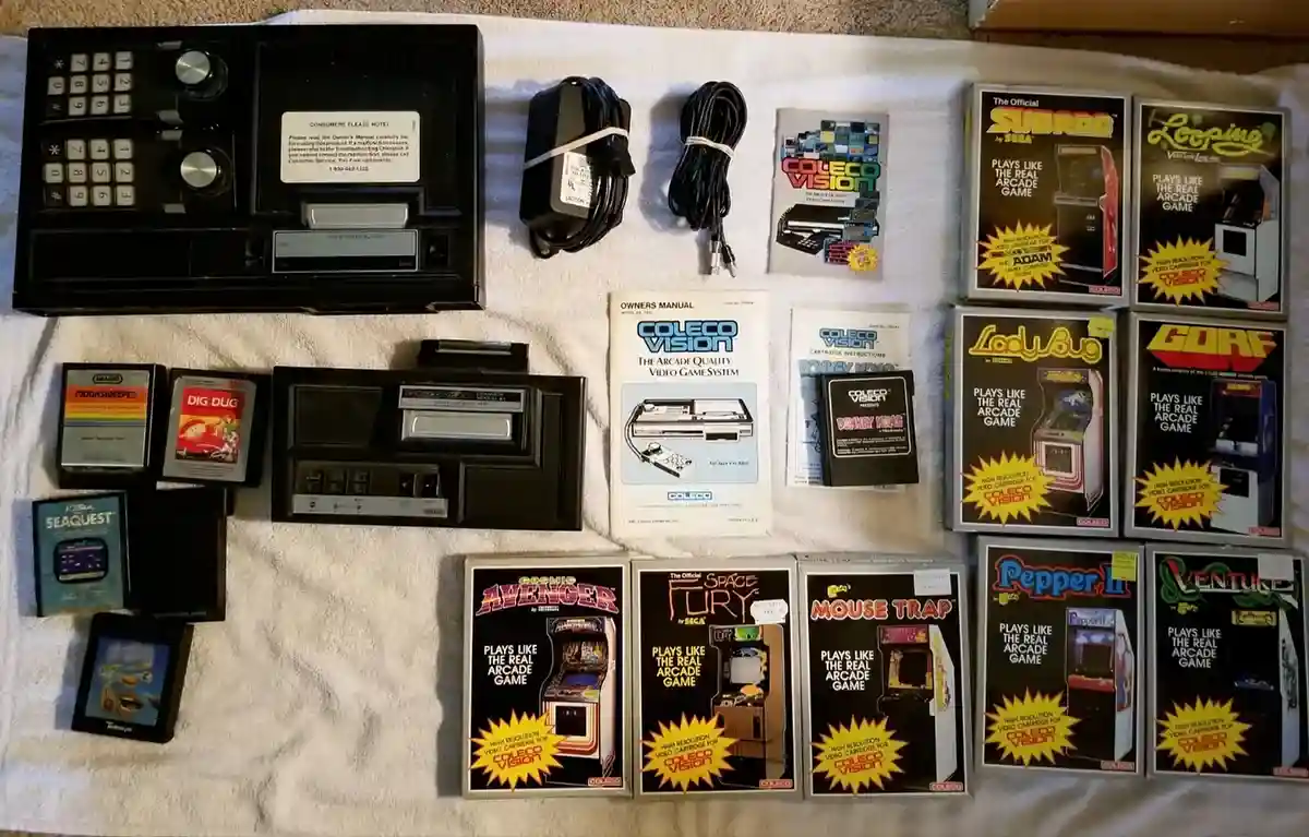 An overhead shot displays a complete ColecoVision video game system, including the console, power adapter, cables, manual…