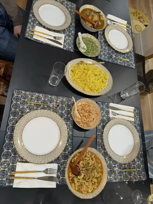 An overhead shot of a formally set dining table with four place settings, each with a white plate, gold-rimmed charger, and…