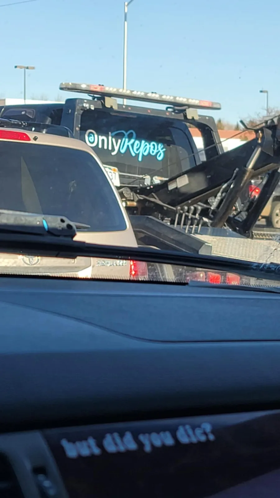 A photo taken from inside a car shows a tow truck with 'Only Repos' written in blue cursive on its rear window. The car's…