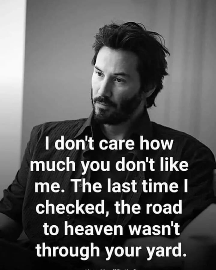 A black-and-white photo of actor Keanu Reeves looking off to the side with a calm, slightly smug expression. Large white…