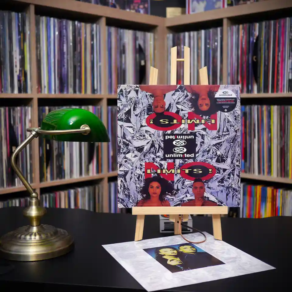 A vinyl record album cover for 'No Limits!' by S2 Unlimited is displayed upright on a small wooden easel on a black table…