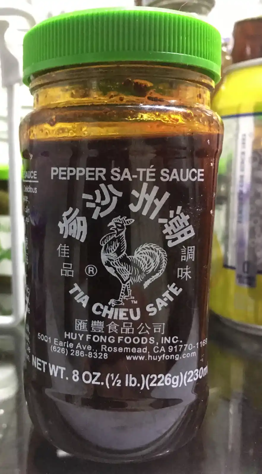 A close-up photo of a glass jar with a green lid containing dark brown sauce, labeled 'PEPPER SA-TÉ SAUCE' and featuring a…