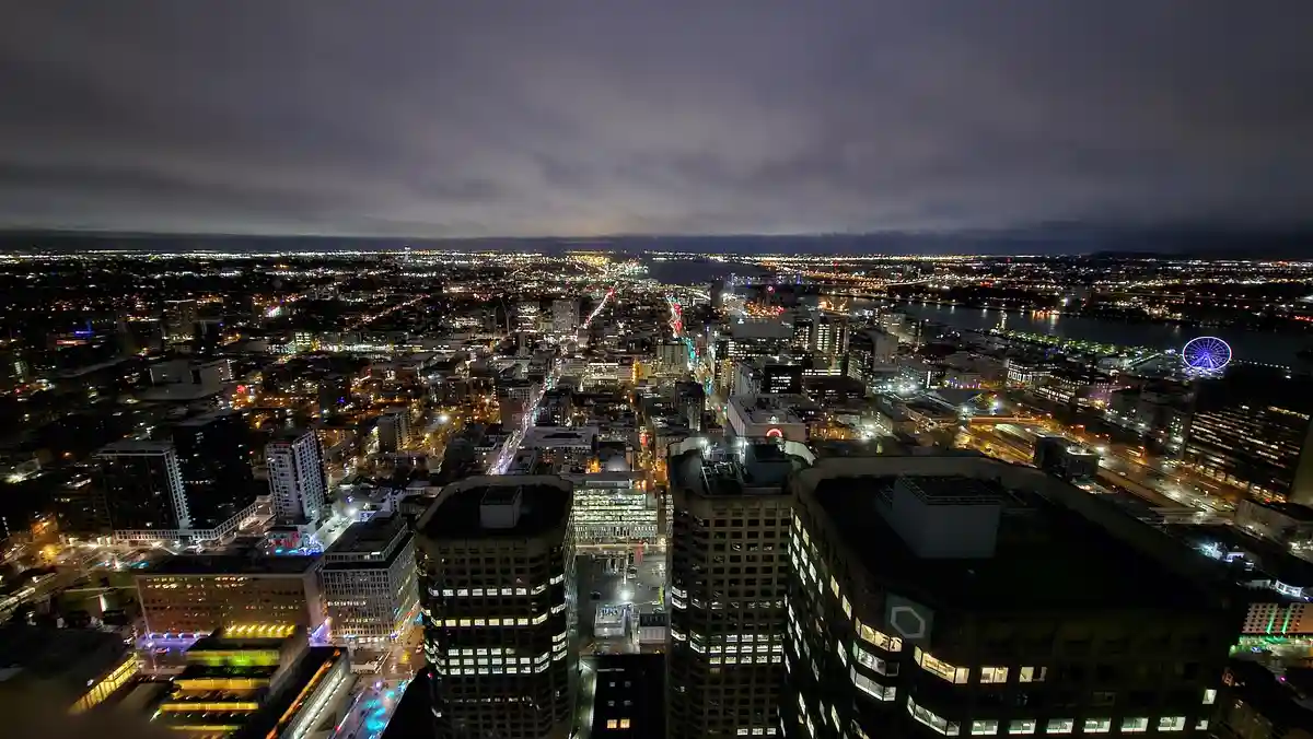 A nighttime aerial photograph of a sprawling cityscape with illuminated buildings, streets, and a large Ferris wheel visible…