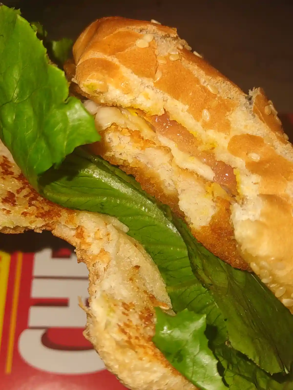 A close-up photo of a partially eaten sandwich with sesame seed bun, lettuce, and a fried patty, with the text 'i'm not a…