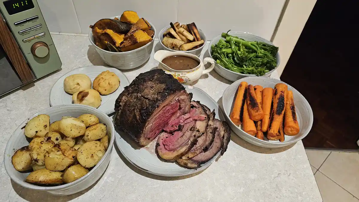 A kitchen counter displays a lavish spread of roast beef, sliced to reveal pink interior, surrounded by bowls of roasted…