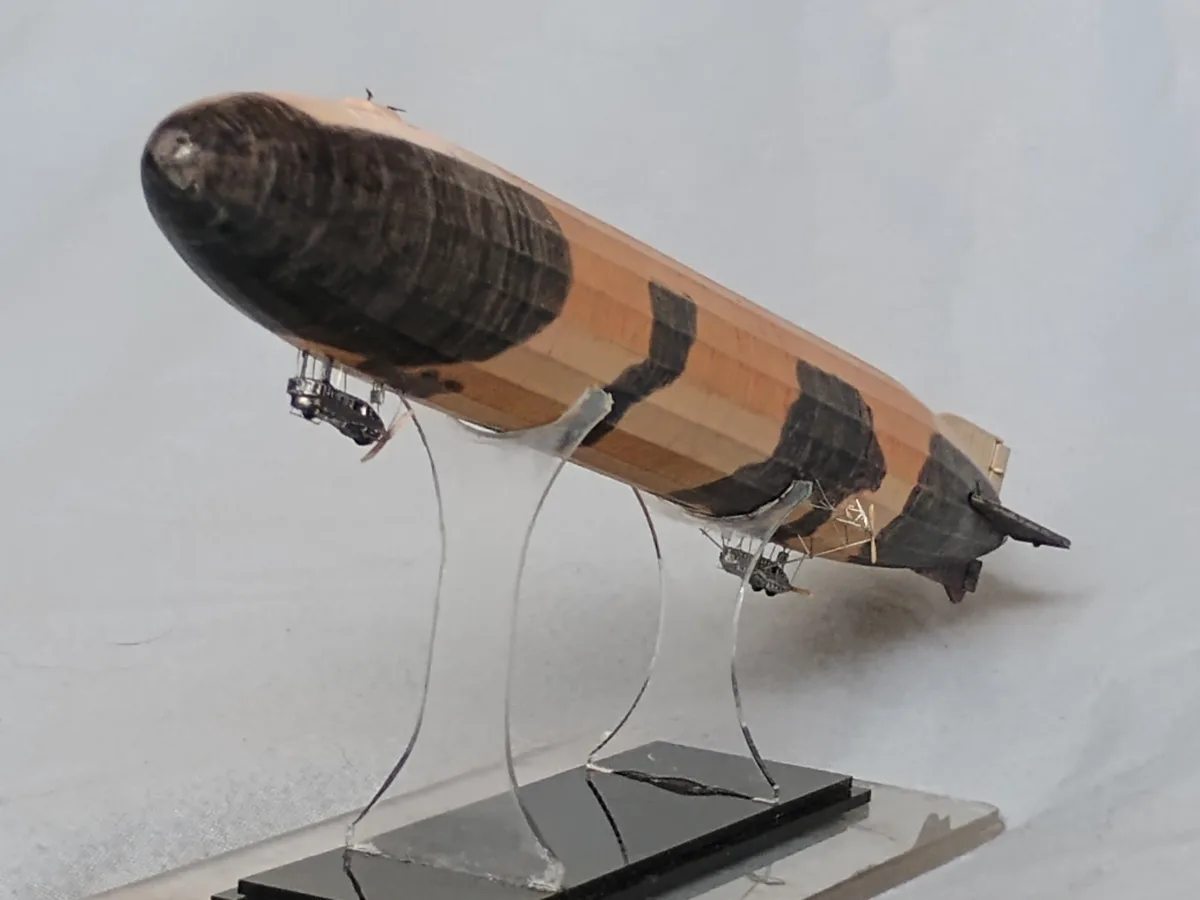 a model zeppelin is displayed on a clear acrylic stand, crafted from a wooden pencil with black graphite markings resembling…