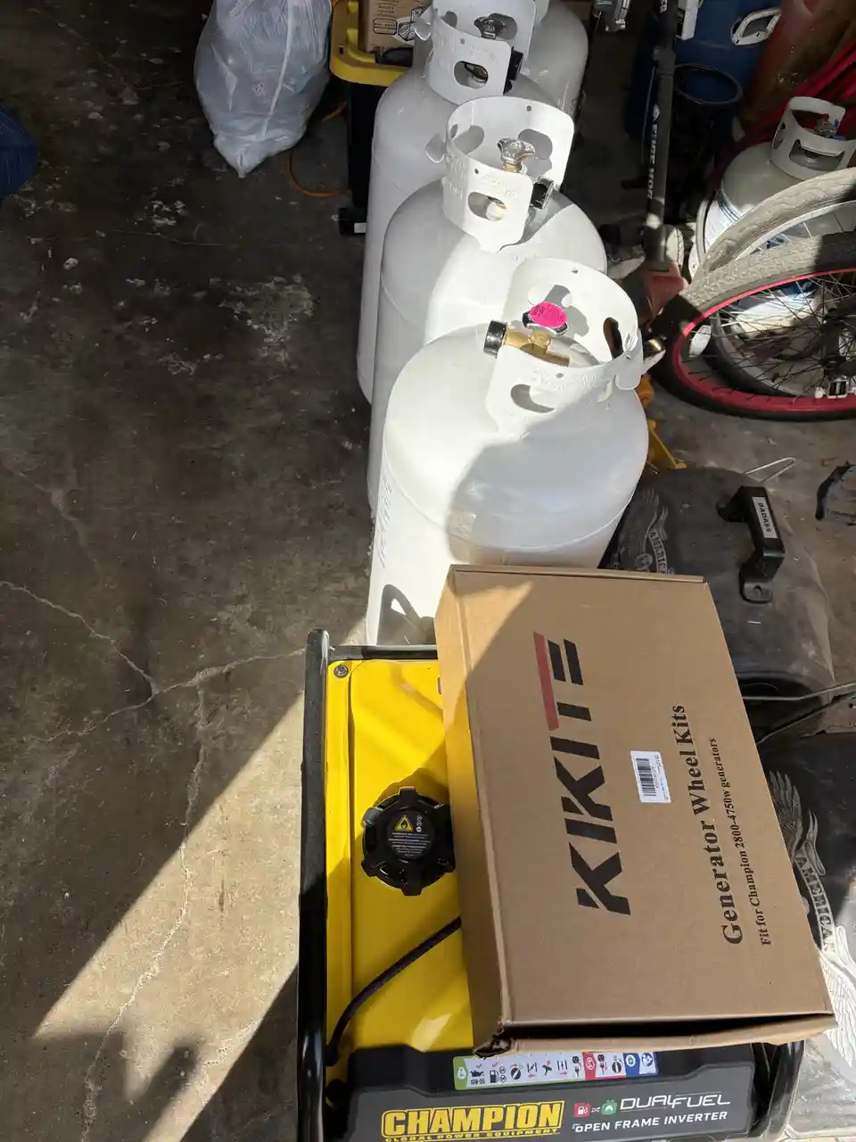 A yellow Champion generator sits on a concrete floor with a cardboard box labeled 'Generator Wheel Kits' resting on top of…