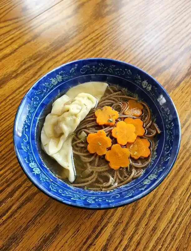 A top-down photo shows a blue ceramic bowl with white floral patterns, resting on a wooden table. Inside the bowl is a dark…