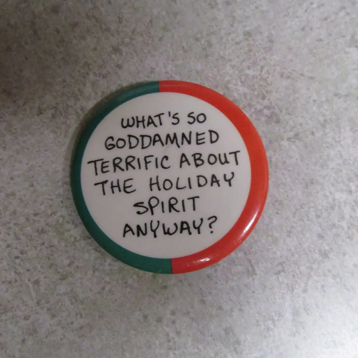 A round button with a red and green border sits on a speckled countertop. The white center has black handwritten text…