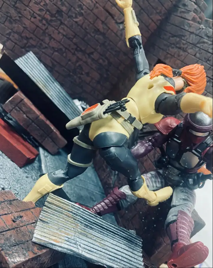 A toy action figure with orange hair and a yellow and black outfit is shown mid-air, seemingly falling or being thrown…