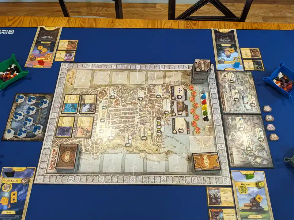 An overhead photo of a 'Dungeons & Dragons: Lords of Waterdeep' board game setup on a blue table mat, showing the central…