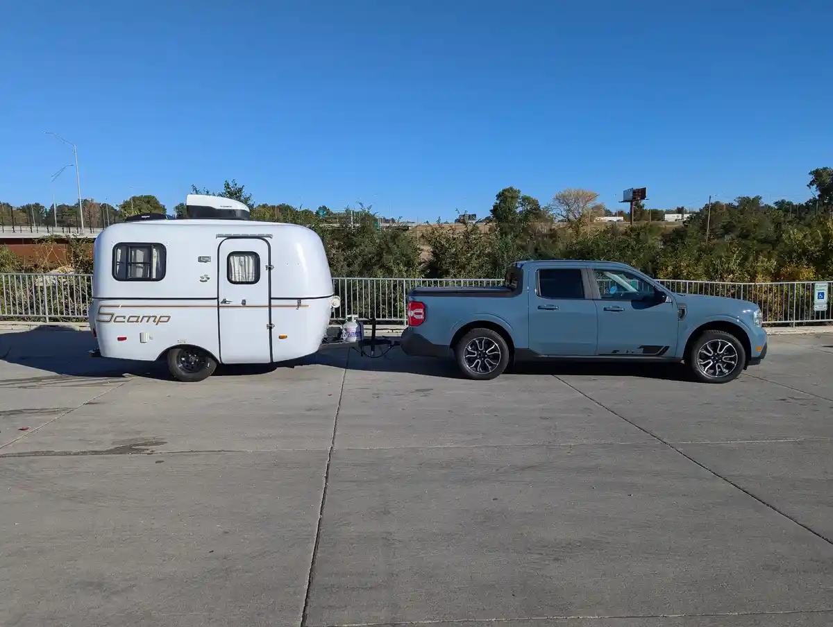 A light blue Ford pickup truck is parked on a concrete lot, hitched to a small white teardrop camper trailer labeled…