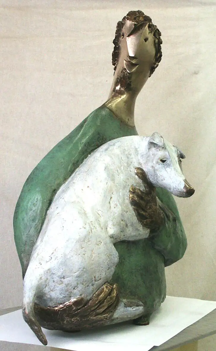 A sculpture depicts a stylized human figure with a green robe and gold face and hands, holding a white dog statue. The human…
