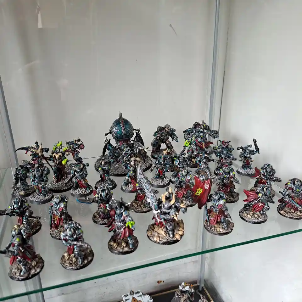 A glass display case holds dozens of intricately painted fantasy miniatures, mostly in dark blue, silver, and red armor with…