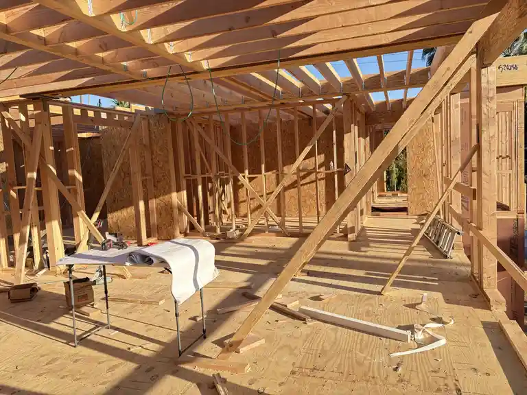 A photo of an unfinished wooden house frame with exposed beams, OSB walls, and construction tools on the floor. A folding…