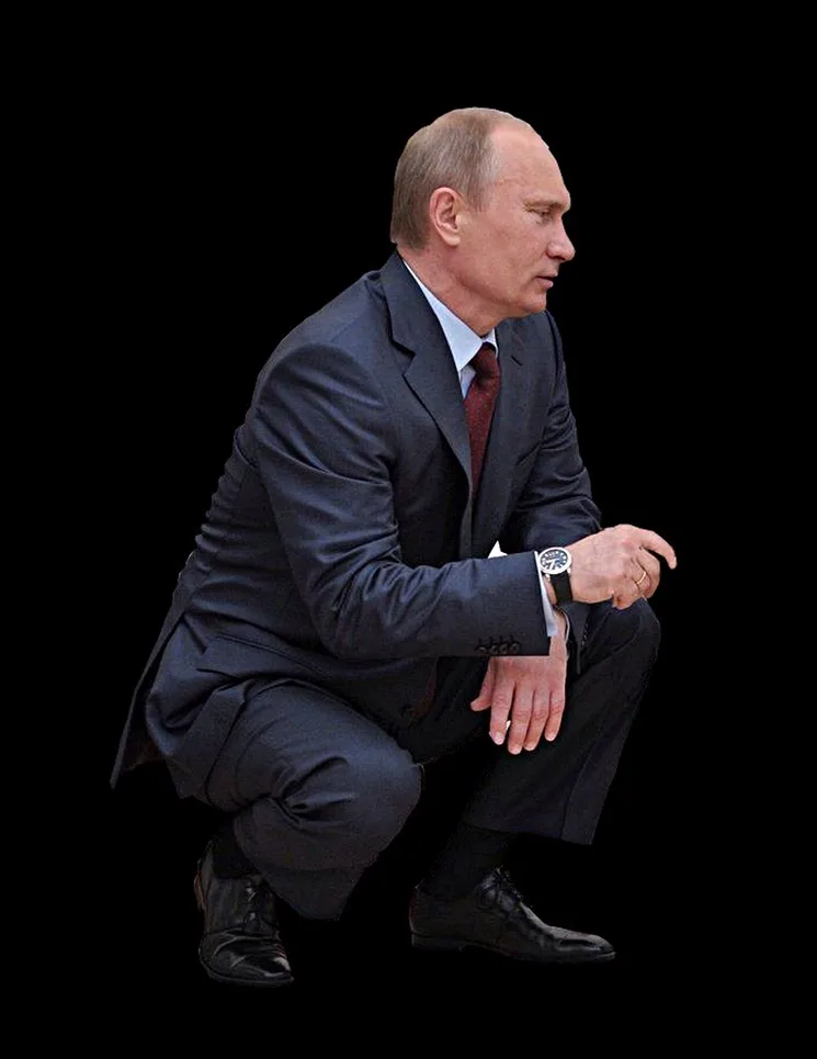 a man in a dark suit and red tie is crouching against a black background, looking off to the side. He wears a watch on his…
