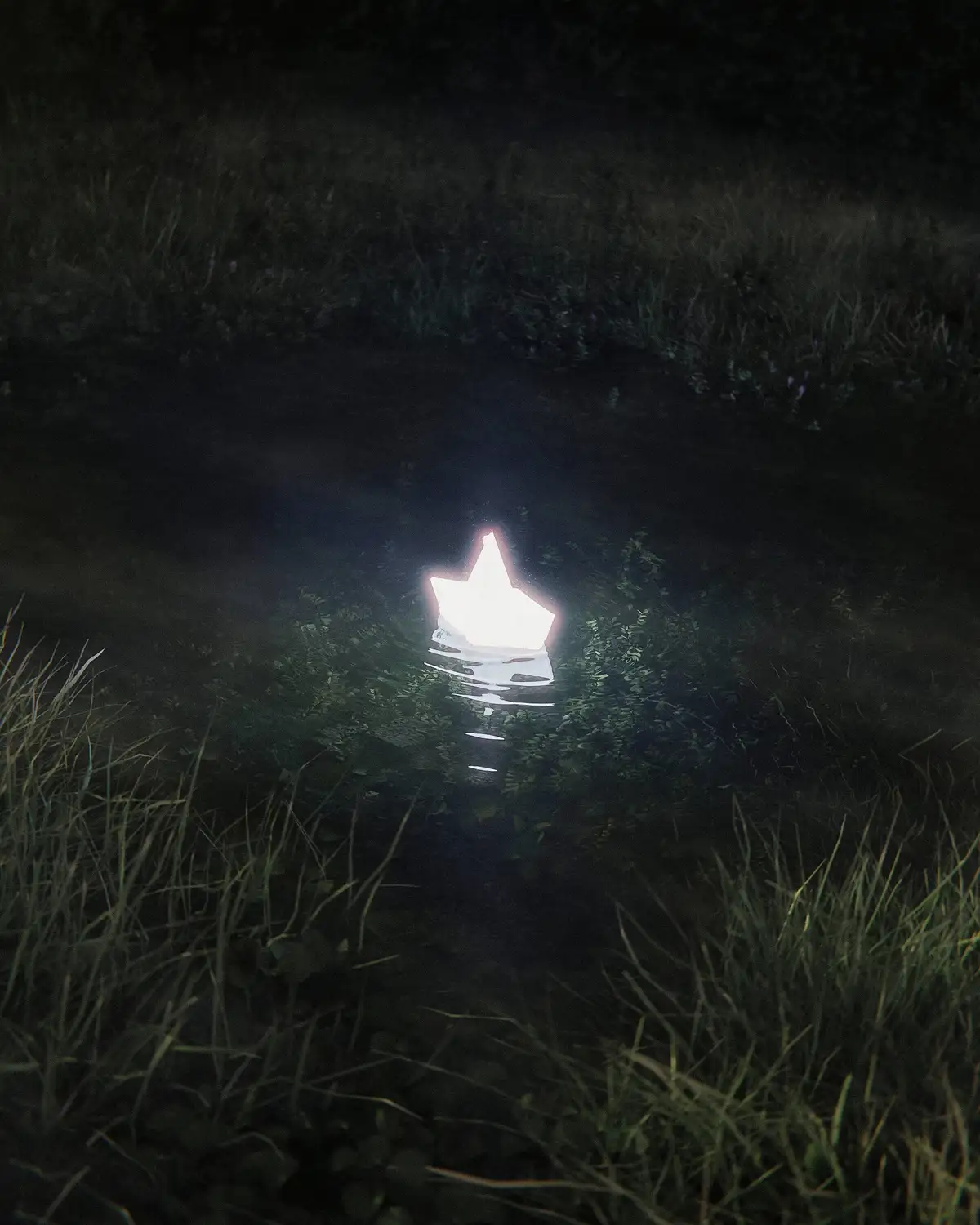A glowing, white, star-shaped lantern floats on dark water at night, surrounded by grassy banks. The overlaid text reads 'i…