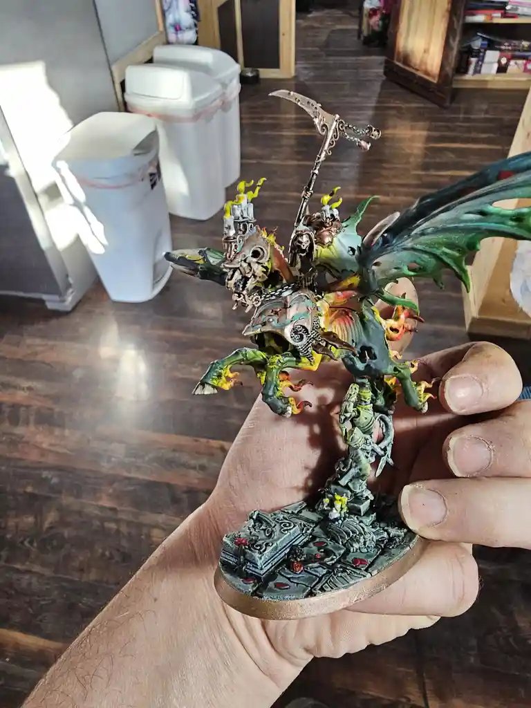 A person holds a highly detailed, intricately painted fantasy miniature of a monstrous, winged creature wielding a scythe…