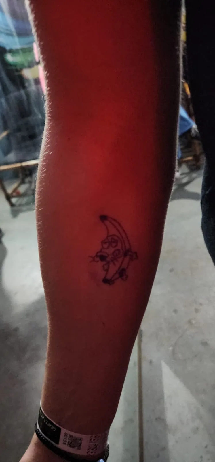 A close-up photo shows a small, simple black ink tattoo on a person's inner forearm. The tattoo depicts a cartoon-style…