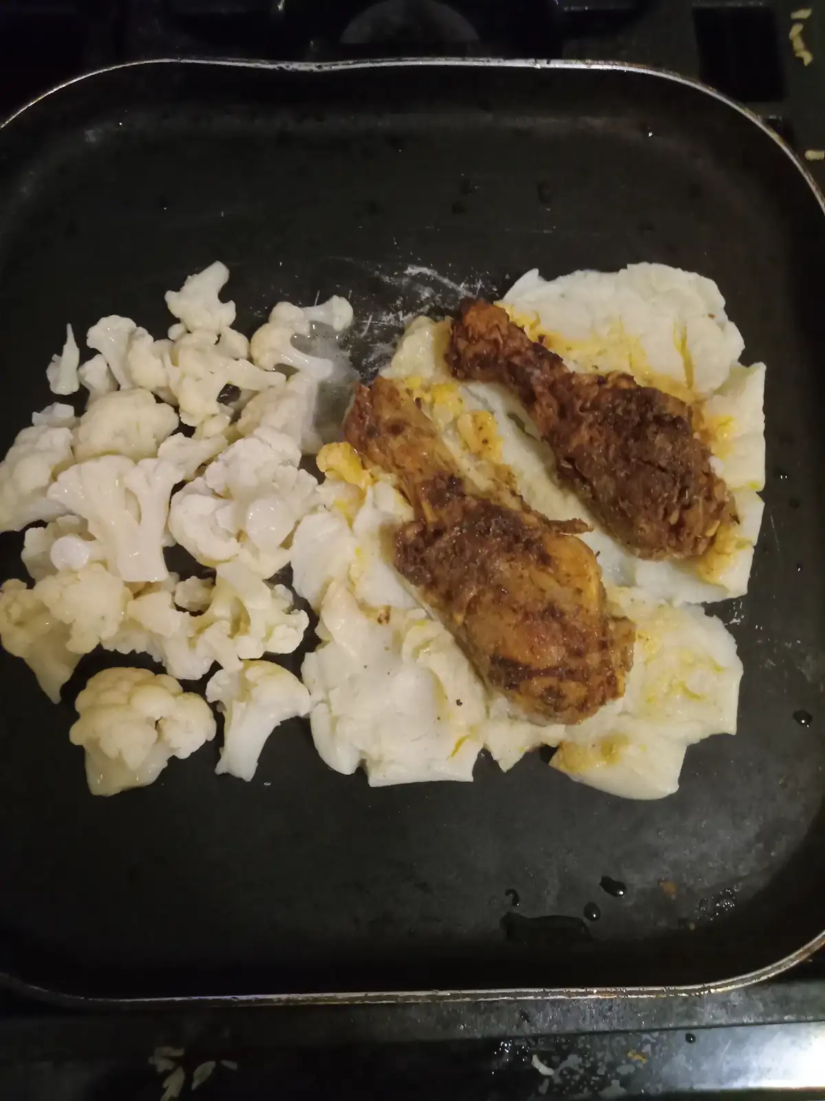 A black frying pan contains two distinct food sections: on the left, florets of raw cauliflower, and on the right, two fried…