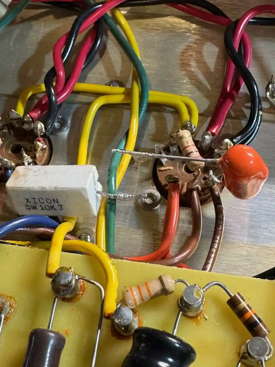 A close-up photo of a messy, vintage electronic circuit board with colorful wires, resistors, and a ceramic component…