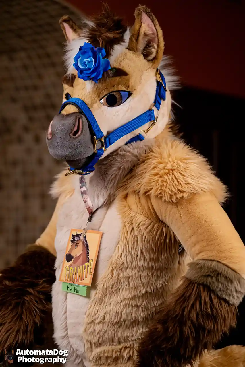 A person in a detailed, tan and brown horse fursuit with a blue halter and a blue rose in their hair, wearing a name tag…