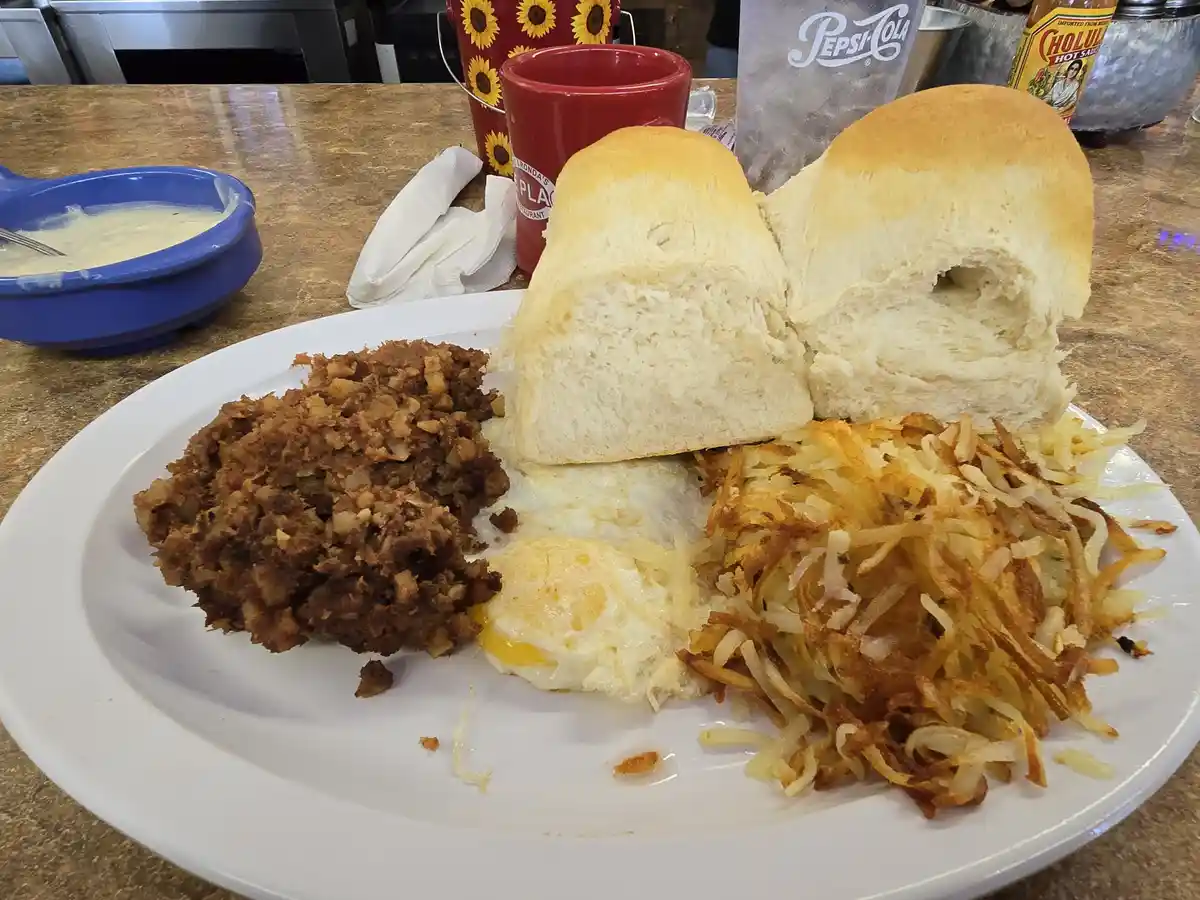 A plate of breakfast food including two halves of a white bread roll, fried eggs, hash browns, and a serving of hash browns…