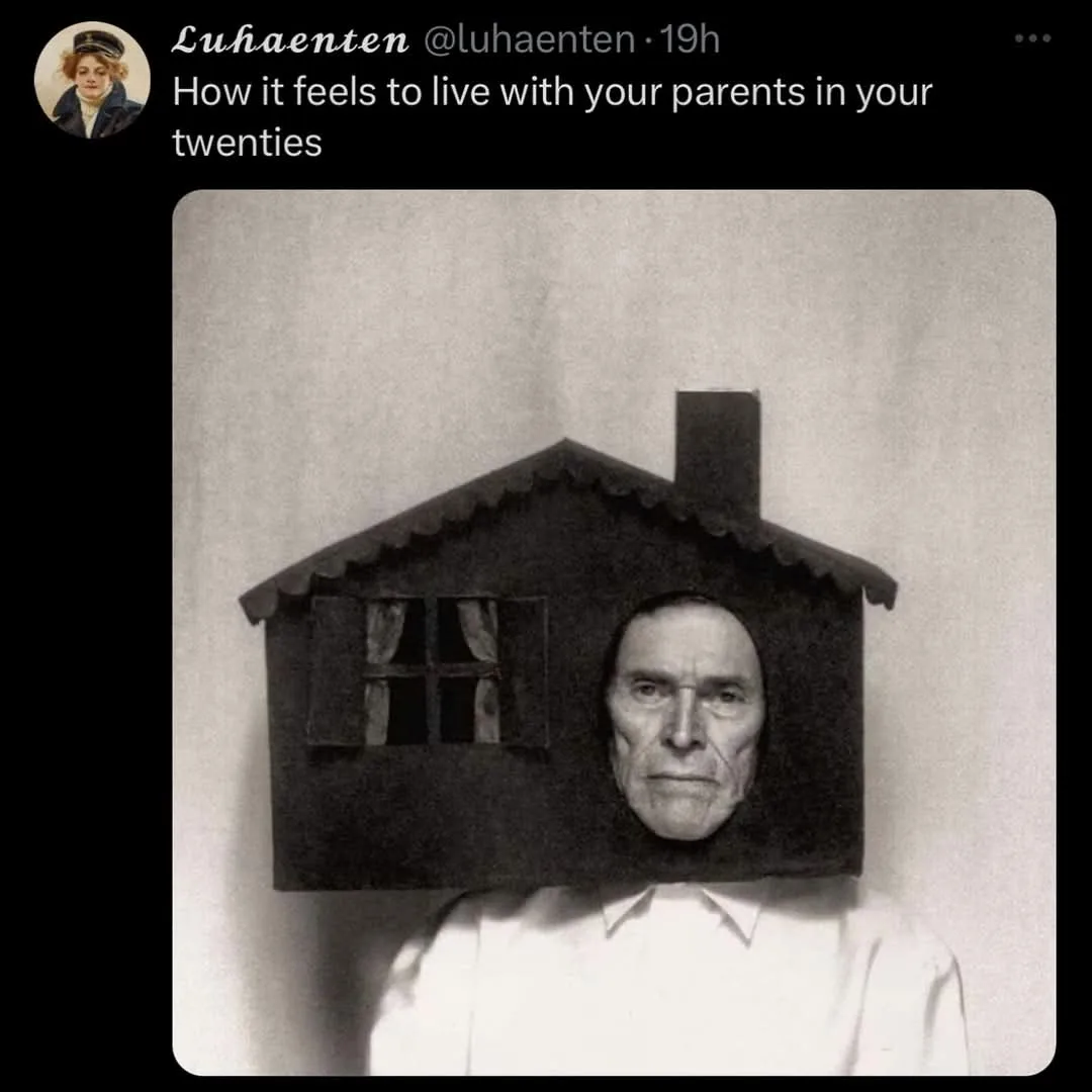 A black-and-white photo shows a man wearing a small house-shaped prop on his head, with a window and chimney visible. The…